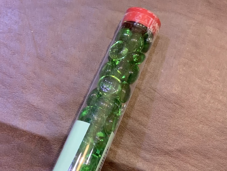 May include: A clear glass tube filled with green glass marbles. The tube has a red lid.