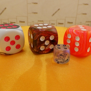 May include: Four dice with different colors and patterns. One die is black and white with red dots, one is brown and red with white dots, one is orange and red with white dots, and one is clear with black dots and text.