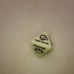 May include: A white, six-sided die with black weather symbols. The die has the words "Light Clouds" and "Storming" printed on it.