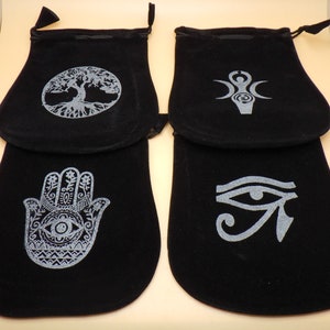 May include: Four black velvet drawstring pouches with different silver embroidered designs. The designs include a tree of life, a triple moon symbol, a hamsa hand, and an eye of Horus.