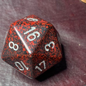 May include: A red and black speckled 20-sided die with white numbers. The die is showing the number 17.