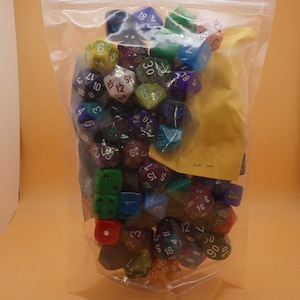 May include: A clear plastic bag filled with a variety of colorful dice. The dice are made of different materials, including plastic and metal. The dice are numbered with white numbers.