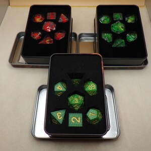 May include: Three metal tins containing sets of green and red dice with gold numbers. The dice are in a starburst pattern inside the tins.
