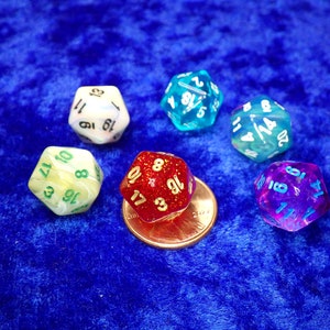 May include: Six multi-sided dice in various colors, including red, blue, green, and purple, are displayed on a blue surface. The dice are numbered and appear to be for tabletop games. A penny is included for size comparison.