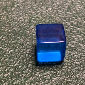 May include: A small, translucent blue cube. The cube is made of plastic and has a smooth, shiny surface.