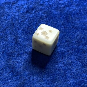 May include: A white dice with black dots on each side. The dice is sitting on a blue surface.