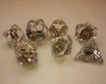 May include: Set of seven clear dice with gold numbers and gears inside. The dice are in various shapes, including a pyramid, a cube, and a dodecahedron.