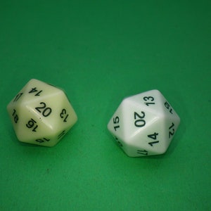 May include: Two twenty-sided dice, one off-white and one bright white, each featuring black numerical markings. The dice are polyhedral in shape with multiple triangular faces, displaying numbers including 12, 13, 14, 15, 16, 17, 18, 19, and 20.