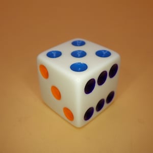 May include: A white dice with blue and orange dots. The dice is showing the number four.
