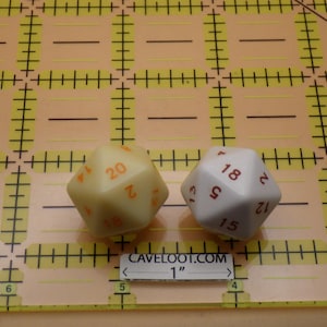 May include: Two multi-sided dice, one cream-colored with orange numbers and the other white with red numbers, are displayed on a yellow grid. The text "CAVELOOT.COM" and "1" are visible.