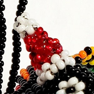 May include: A beaded ornament featuring a red, white and black design. The ornament is crafted from small, colourful beads that are strung together to create a distinctive and intricate pattern.