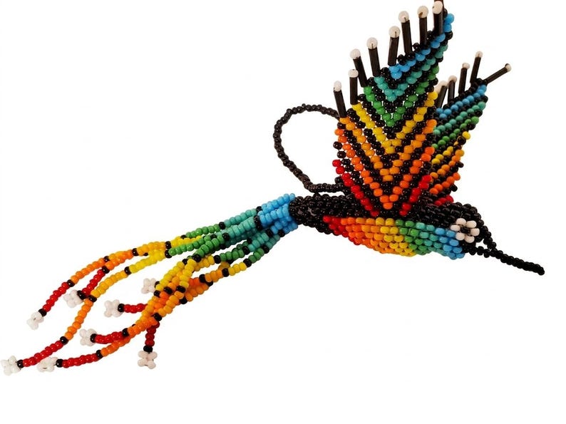 May include: A handcrafted, beaded hummingbird in flight. The bird features a vibrant array of colors, including blue, green, yellow, orange, and red, with black accents. The wings are spread, and the tail feathers are long and flowing.
