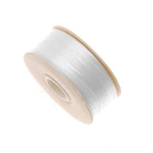 May include: A spool of white thread with a light brown cardboard core. The thread is tightly wound, and the spool is angled slightly to the left against a white background. The thread appears to be a fine, smooth material.