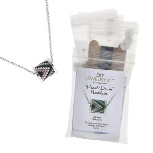 Puede incluir: Collar plateado con un colgante cilíndrico de cuentas en negro, gris y rosa. En el fondo, un kit de joyería DIY con el texto "Heart Drum Necklace". El kit incluye instrucciones, cuentas, abalorios y cadena.