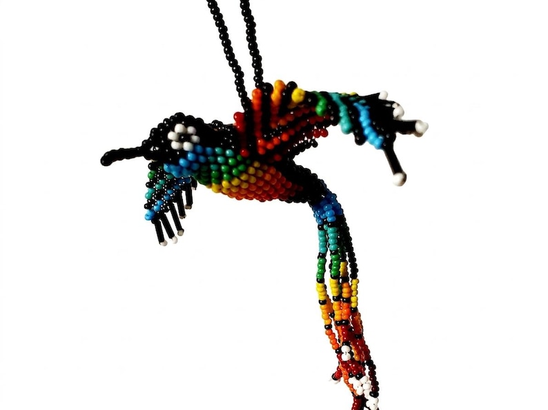 May include: A handcrafted hummingbird pendant necklace made of colorful beads. The bird features a black beak, head, and tail, with a body of rainbow-colored beads. The necklace is suspended from a black beaded chain.