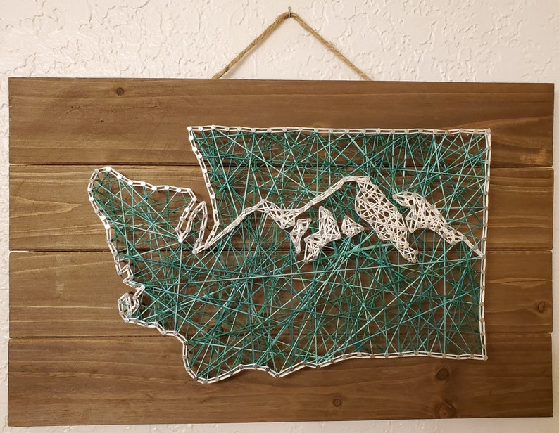 Puede incluir: Una pieza de arte de pared de madera con un dise&ntilde;o de arte de cuerda que representa el estado de Washington. El contorno del estado est&aacute; creado con cuerda blanca, y las monta&ntilde;as est&aacute;n rellenas con cuerda turquesa.