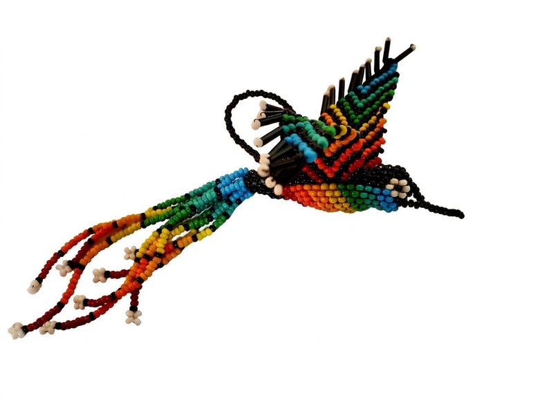 May include: A handcrafted hummingbird ornament made of colorful beads. The bird features a rainbow of colors, including blue, green, orange, and red, with a black body and tail. The hummingbird is designed with a curved beak and outstretched wings.