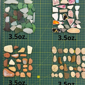 May include: Four separate piles of sea glass, sea shells, and stones, each weighing 3.5 ounces. The piles are arranged on a green cutting mat with a grid pattern.