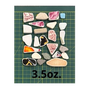May include: A collection of assorted ceramic shards and sea glass pieces in various shapes, colors, and patterns, including white, pink, black, orange, and textured grey fragments. The pieces are arranged on a grid, with the text 3.5oz. visible.