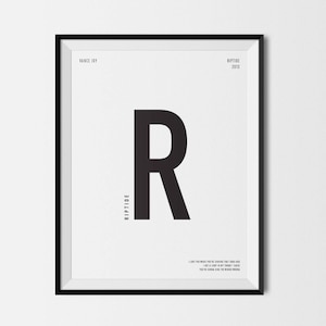 May include: A framed black and white art print featuring a large black letter "R" centered on a white background. The print includes the text "Vance Joy" and "Riptide 2013" at the top, with the word "Riptide" vertically along the left side. A quote is at the bottom.