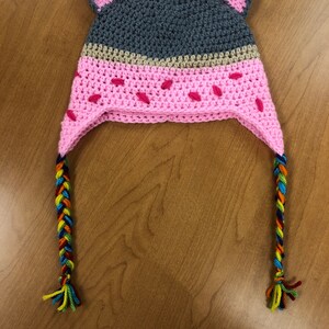 May include: Gray and pink crocheted hat with cat ears and colorful braided ties.