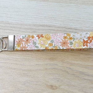 May include: A white key chain with a floral pattern in shades of orange, yellow, and pink. The key chain has a silver metal ring.