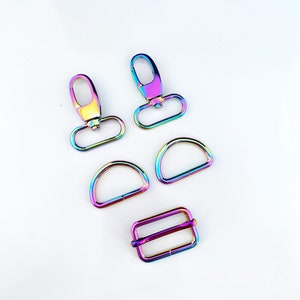 May include: A set of five rainbow-colored metal hardware pieces for crafting. The set includes two swivel clasps, two D-rings, and one slider buckle.
