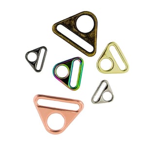 May include: A collection of six triangular metal strap adjusters in various finishes, including antique brass, polished gold, iridescent rainbow, rose gold, silver, and black, each featuring a circular opening and a rectangular slot.