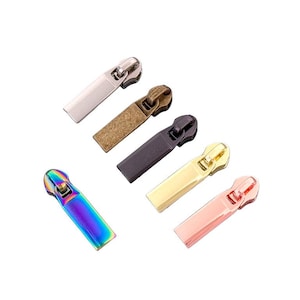 May include: A collection of metal zipper pulls in various colors, including silver, bronze, black, gold, rose gold, and iridescent rainbow. The pulls are rectangular with a curved top and a loop for attaching to a zipper.