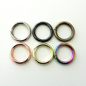 May include: Six round metal spring gate rings in various colors: silver, black, antique brass, rose gold, gold, and iridescent rainbow. These rings are used for attaching items.