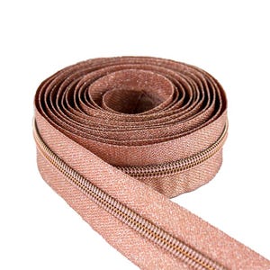 May include: A roll of rose gold zipper tape with a metallic finish. The zipper tape is coiled and ready to be used for sewing projects.