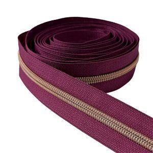 May include: A continuous roll of deep burgundy zipper tape featuring a metallic gold-toned coil. The zipper tape is coiled into a circular shape with one end extending outward, showcasing the textured fabric edges and the central interlocking teeth.
