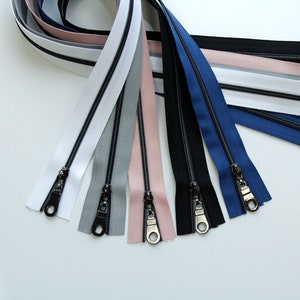 May include: A set of seven zipper tapes in various colors, including white, gray, pink, black, and blue. The zippers have black metal sliders.
