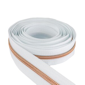 May include: A roll of white zipper tape with a metallic rose gold zipper. The zipper is coiled and ready for use in sewing projects. The white tape has a textured surface.