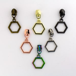May include: Six zipper pulls with hexagonal charms in different colors: antique brass, gold, black, rose gold, and iridescent.