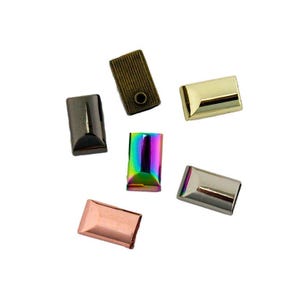 May include: A collection of six rectangular metal cord ends in various finishes including antique bronze with a textured surface, polished gold, iridescent rainbow, matte black, brushed silver, and a smooth copper tone.