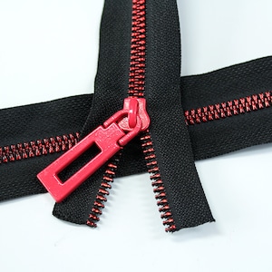 May include: A black zipper with red stitching and a pink zipper pull. The zipper is open and the two sides are laying flat.