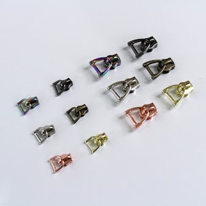 May include: Assortment of zipper pulls in various colors and finishes, including silver, gold, black, and rainbow. The zipper pulls are in the shape of a small, open-ended rectangle with a rounded top.