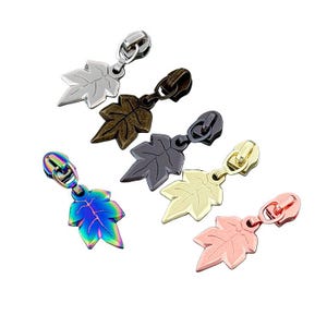 May include: A collection of decorative zipper pulls in various metallic finishes. Each pull features a leaf-shaped charm attached to a metal zipper. Colors include silver, bronze, gunmetal, gold, iridescent, and rose gold.