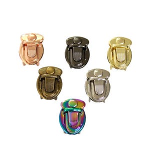 May include: A collection of six metal bag locks in various finishes, including rose gold, gunmetal, gold, antique brass, silver, and an iridescent rainbow finish. Each lock features a rounded top and a vertical ribbed push-button release.