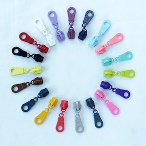 May include: Assortment of colorful zipper pulls in various colors, including red, blue, green, yellow, and purple. The zipper pulls are arranged in a circle on a white background.