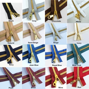May include: Assortment of 16 colors of zipper tape with gold metal zipper pulls. The zipper tape is laid out in a grid pattern with each color labeled below.