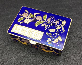May include: A small blue enamel box with gold trim and a floral design. The box has a white label with the text "真 僪 匊" in black.