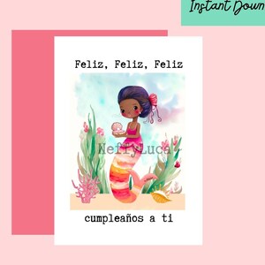 May include: A birthday card featuring a watercolor illustration of a mermaid with brown skin and pink hair holding a seashell. The card has the text "Feliz, Feliz, Feliz cumplea&ntilde;os a ti" in black.