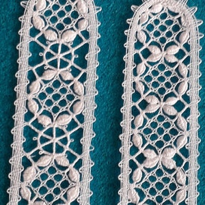 Op de afbeelding: Twee witte kant-bladwijzers met een delicaat bloemenpatroon. De bladwijzers bevinden zich op een turquoise achtergrond.
