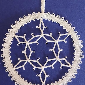 May include: A white, circular, handmade lace ornament with a snowflake design. The ornament is suspended by a white string against a blue background. The lace features a detailed, openwork pattern.
