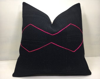 May include: Black pillow with a pink diamond pattern. The pillow is made of a textured fabric and has a simple, modern design.