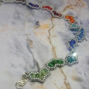 May include: A rainbow-coloured beaded bracelet with silver beads and a silver clasp. The bracelet is made of small, faceted beads that are arranged in a zig-zag pattern.