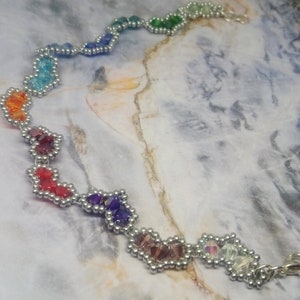 May include: A rainbow-coloured beaded bracelet with a silver clasp. The beads are arranged in a heart shape and are connected by silver wire.