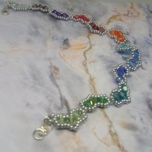 May include: A rainbow-coloured beaded bracelet with silver accents. The beads are arranged in a heart shape and are connected by silver wire.